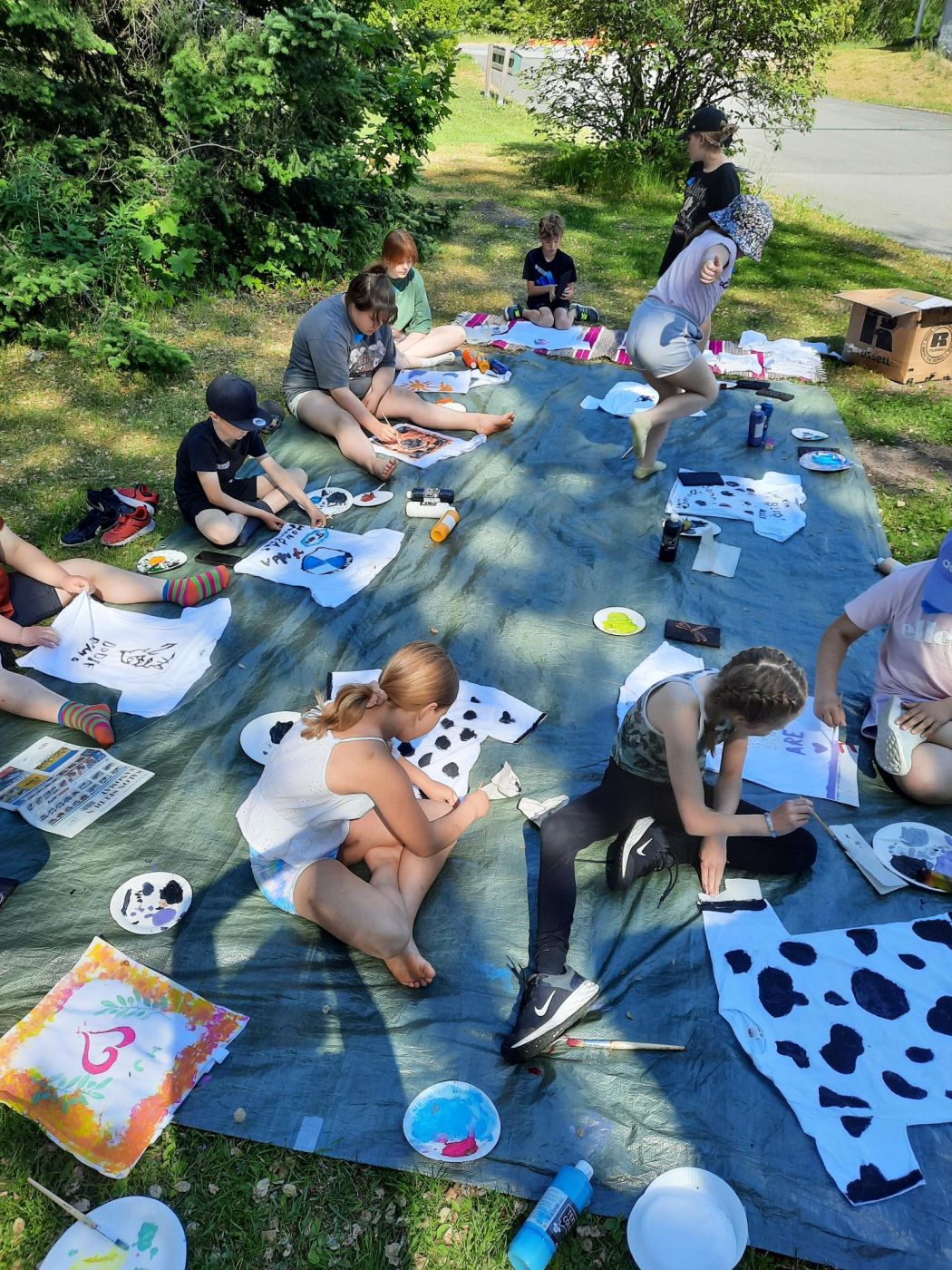 Leiriläiset maalaamassa t-paitoja ulkona