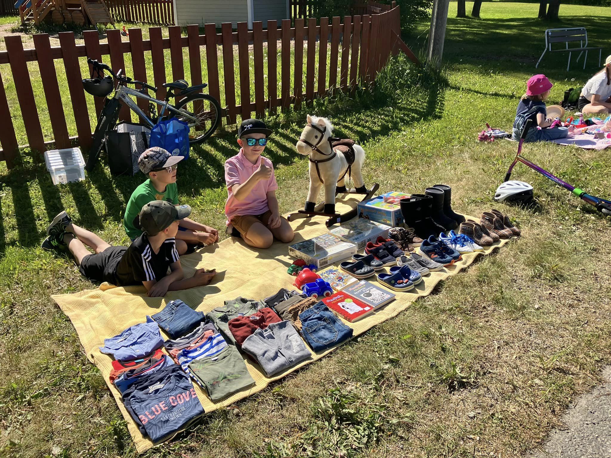 Kuvassa vilttiskirppiksen yksi myyntipiste, jossa kolme lasta myymässä vaatteita, kenkiä ja leluja