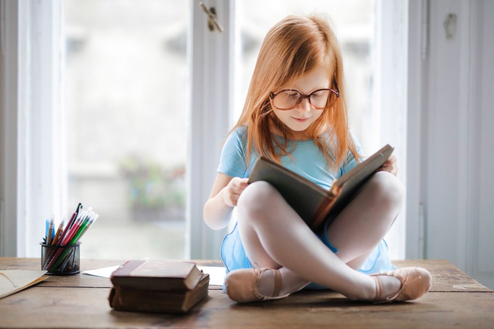 Kuvassa lapsi istuu pöydällä lukemassa kirjaa
